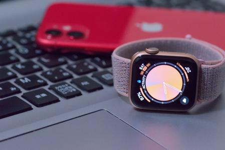 Un Apple Watch en primer plano con un ordenador y un iPhone de fondo.